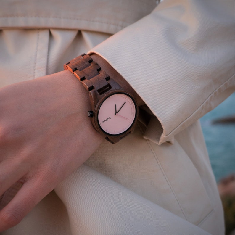 May include: A wooden wristwatch with a brown band and a pink face. The watch face has black hands and the word "ZIMMER" printed on it.