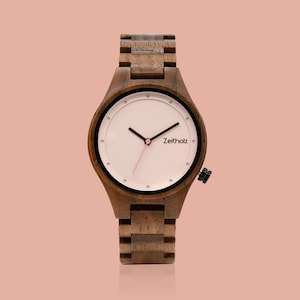 May include: A wooden wristwatch with a brown wooden band and a white face with black hour and minute hands and a pink second hand. The watch face has black markings and the word "Zeitholz" printed on it.