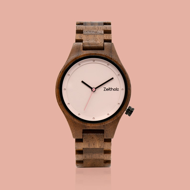 May include: A wooden wristwatch with a brown wooden band and a white face with black hour and minute hands and a pink second hand. The watch face has black markings and the word "Zeitholz" printed on it.