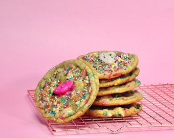 May include: A stack of six colorful sprinkle cookies on a gold wire cooling rack. The top cookie has a pink candy heart on top.