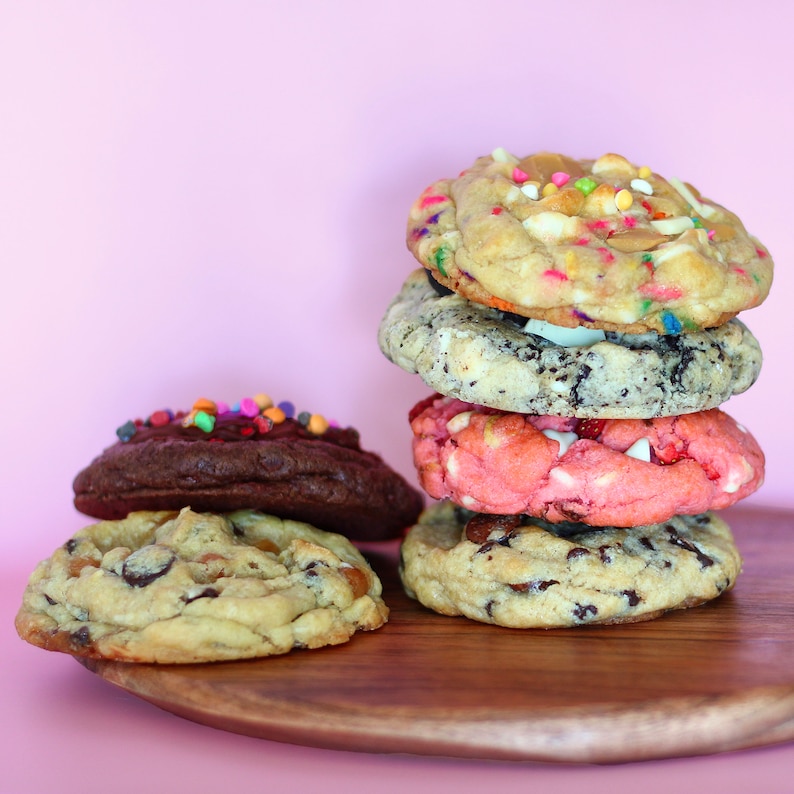 Puede incluir: Una pila de seis galletas de diferentes sabores en una tabla de cortar de madera. Las galletas est&aacute;n dispuestas en forma de torre, con la galleta m&aacute;s grande en la parte inferior y la galleta m&aacute;s peque&ntilde;a en la parte superior. Las galletas son de diferentes colores y tienen varios ingredientes, incluyendo chispas, chispas de chocolate y nueces.