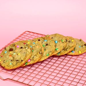 May include: A close-up of six chocolate chip cookies with colourful sprinkles on a pink wire cooling rack.