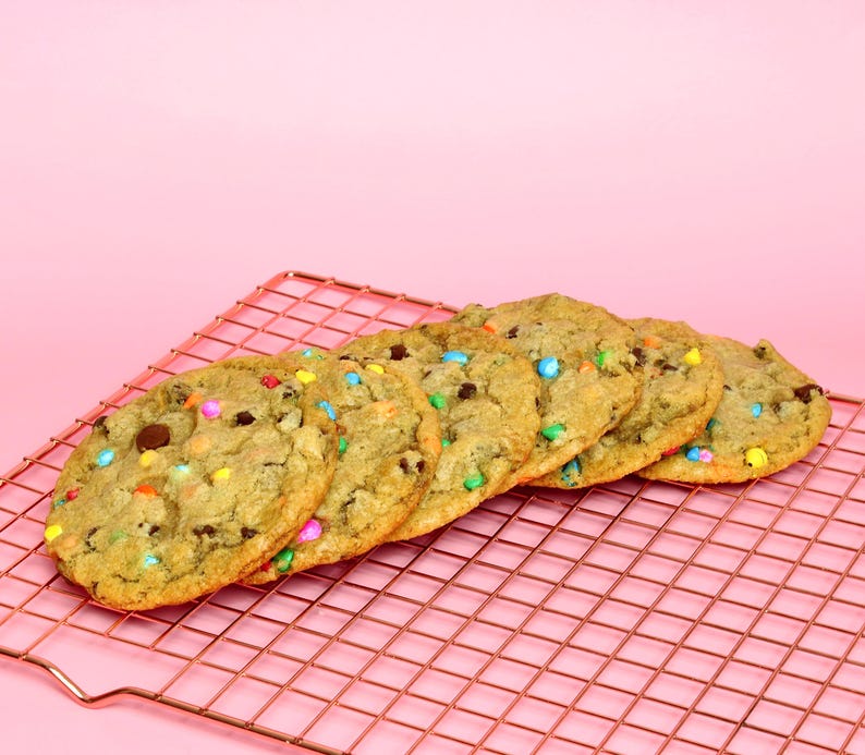 May include: A close-up of six chocolate chip cookies with colourful sprinkles on a pink wire cooling rack.