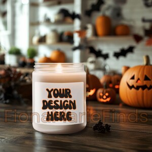 Op de afbeelding: Een brandende kaars in een heldere glazen pot met een wit etiket met de tekst "YOUR DESIGN HERE" in zwarte en oranje letters. De achtergrond toont pompoenen, vleermuizen en Halloween-decoraties.
