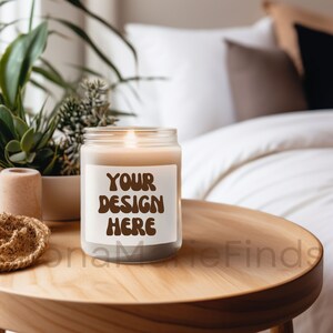 Op de afbeelding: Een glazen kaars pot met een bruin label met de tekst "YOUR DESIGN HERE" op een houten tafel. De kaars is aangestoken en er staat een plant op de achtergrond.