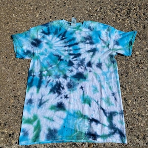 May include: A short-sleeved t-shirt with a tie-dye pattern in shades of blue, green, and white. The shirt has a crew neck and a classic fit. The tie-dye design features swirling patterns and a mix of light and dark hues.