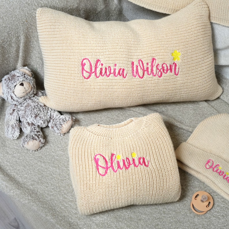 three personalized pillows and a teddy bear on a bed