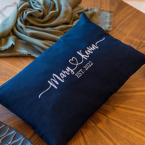 May include: A navy blue throw pillow with white embroidery that reads "Mary & Kevin EST. 2022".
