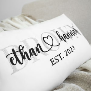 May include: White pillow with black embroidered text that reads "Ethan & Hannah EST. 2023" with a heart symbol between the names.