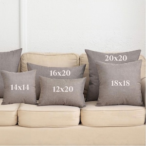 May include: A set of six throw pillows in various sizes, all in a light brown color. The pillows are arranged on a beige couch. The pillows are labeled with their dimensions in inches: 14x14, 16x20, 12x20, 18x18, and 20x20.