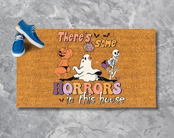 May include: A rectangular doormat with the text "There's some HORRORS in this house" and Halloween-themed graphics. The design includes a pumpkin, ghost, and skeleton. A pair of blue shoes with white laces are on the left.