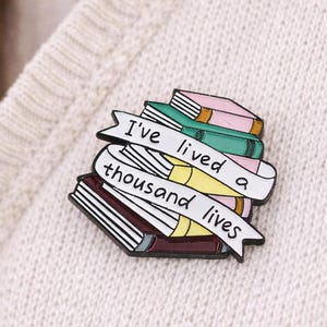 Broche de esmalte em forma de pilha de livros com a frase "Eu vivi mil vidas".