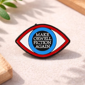 Könnte beinhalten: Eine Anstecknadel in Form eines Auges mit einem rot-weiß-blauen Design. Der Text "MAKE ORWELL FICTION AGAIN" ist im blauen Kreis zentriert. Die Anstecknadel hat einen schwarzen Rand.