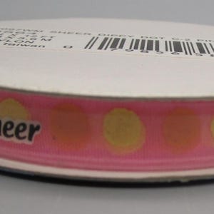 May include: A spool of pink sheer ribbon with yellow and orange polka dots. The word "Sheer" is printed in black on the ribbon. The ribbon is 3/8 inch wide and made of 100% nylon.