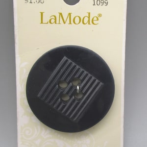 May include: A black, round LaMode button with four holes and a textured, ridged design. The button is attached to a cream-colored card with the LaMode logo and the number 1099.