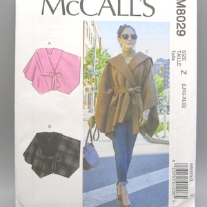 May include: McCall's sewing pattern M8029 featuring a cape design. The pattern includes illustrations of a pink cape with a tie, a plaid cape, and a woman wearing a brown cape with a hood and belt. Size Z (LRG-XLG).