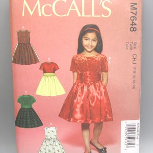 May include: McCall's sewing pattern M7648 for girls' dresses. The pattern features illustrations of various dress designs, including a red dress worn by a girl. The pattern includes size CHJ (7-8-10-12-14). Designed and printed in the USA.