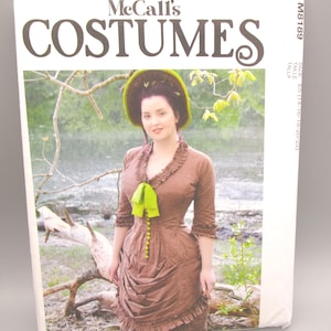 May include: A McCall's Costumes sewing pattern featuring a woman in a brown dress with a green bow and hat. The pattern cover has the text "McCall's COSTUMES" in large letters and the designer's name, "Angela Clayton."
