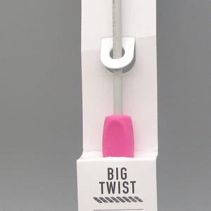 May include: A crochet hook with a pink handle and a silver hook, displayed in a white cardboard package. The package has the text "BIG TWIST" and "CROCHET HOOK US F / 3.75 MM".