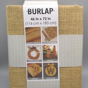 May include: A roll of burlap fabric, measuring 46 inches by 72 inches, is packaged with a label. The label features the word "BURLAP" and images suggesting uses like home decor, gifting, and stenciling. The fabric is a natural material.