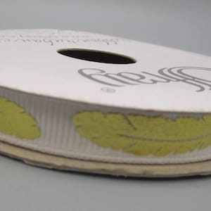 May include: A spool of white ribbon with a repeating pattern of yellow-green feathers. The ribbon is on a cardboard spool with the brand name "Offray" printed on the top. The ribbon is suitable for crafts and gift wrapping.