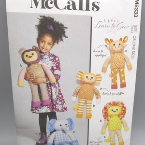 May include: McCall's sewing pattern for stuffed animals. The pattern includes instructions to create a monkey, giraffe, elephant, and lion. The pattern is designed for beginners and is fat-quarter friendly. The image shows a young girl holding a finished monkey.