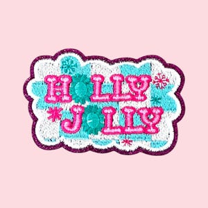 Może przedstawiać: Haftowana naszywka z napisem "HOLLY JOLLY" w kolorze różowym, turkusowym i białym. Naszywka ma biało-turkusowe, w kratkę tło z akcentami płatków śniegu i kwiatów. Naszywka ma fioletową, brokatową obwódkę.