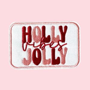 Może przedstawiać: Haftowana naszywka z napisem "Holly Vibes Jolly" w czerwonych i różowych literach. Naszywka ma białe tło i różową obwódkę, idealna do dodania do odzieży lub akcesoriów.