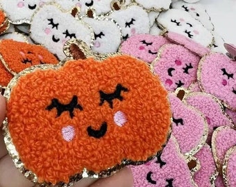 May include: A collection of felt pumpkin patches with embroidered faces. The pumpkins are in white, pink, and orange with gold glitter trim.