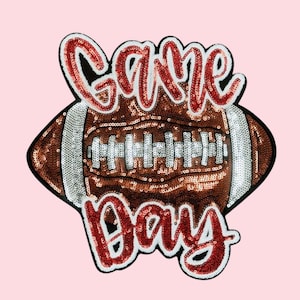 May include: A sequined patch in the shape of a football with the words "Game Day" in red sequins. The football is brown with white stripes and details, set against a light pink background.