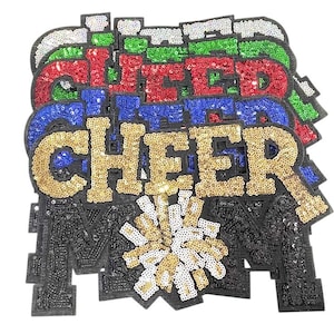 May include: A collection of sequined patches spelling "CHEER" in gold, blue, red, green, and white. The bottom patch features a black "M" with a gold and white pom-pom design. These patches are likely for cheerleading apparel.
