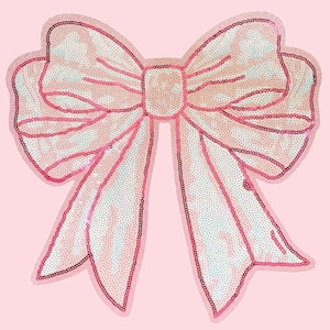 Puede incluir: Un gran lazo decorativo en tonos rosas, adornado con lentejuelas. El lazo tiene un centro rosa claro y está delineado con un rosa más oscuro. El fondo es rosa liso y suave.