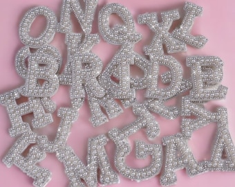 Puede incluir: Un conjunto de letras cubiertas de perlas blancas que deletrean "Bride to Be" sobre un fondo rosa.