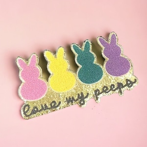 Könnte beinhalten: Ein goldener Glitzer-Patch mit vier bunten Marshmallow-Peeps und dem Text "Love my peeps".