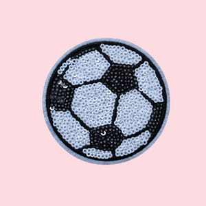 May include: A round, sequined patch in the shape of a soccer ball. The design features black and white pentagons, with a light blue border. The sequins add a shimmering effect to the patch.