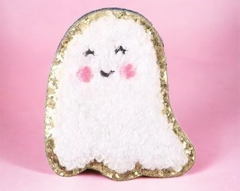 May include: A white fuzzy ghost with a gold glitter outline and a smiling face. The ghost has pink cheeks and black eyes.