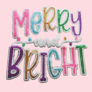 May include: A sequined applique with the words "Merry and Bright" in various colours, including pink, green, gold, and purple, on a light pink background. The letters are outlined in silver.