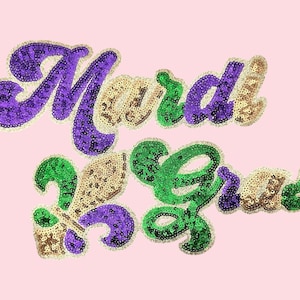 Puede incluir: Texto de Mardi Gras en lentejuelas moradas, verdes y doradas sobre un fondo rosa. El texto está en una fuente cursiva con un símbolo de flor de lis. Las lentejuelas están delineadas con un borde dorado.