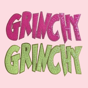 May include: A light pink background with the word "GRINCHY" in pink sequins and again in green sequins. The text is large and bold, with a glittery outline. The overall design is eye-catching.