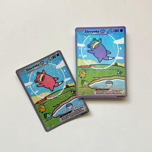 Peut inclure: Deux cartes à collectionner Slowpoke EX. L'une présente un Slowpoke rose, l'autre un Slowpoke violet. Les deux cartes ont un fond bleu avec le texte "Slowpoke EX - 180".