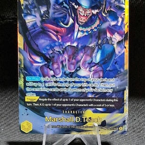 Può includere: Una carta collezionabile di One Piece raffigurante Marshall D. Teach con un livello di potenza di 10000 e un costo di 8. La carta mostra un'illustrazione dinamica del personaggio in toni blu e viola, con testo che descrive gli effetti di gioco.