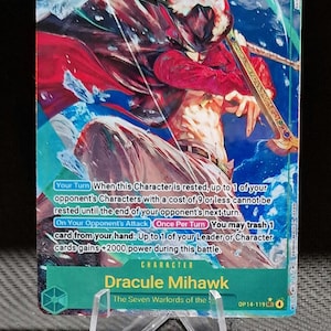 May include: A collectible trading card featuring Dracule Mihawk from "The Seven Warlords of the Sea." The card displays a character illustration with a red and white color scheme, a power level of 10000, and game text. The card is displayed on a clear plastic stand.