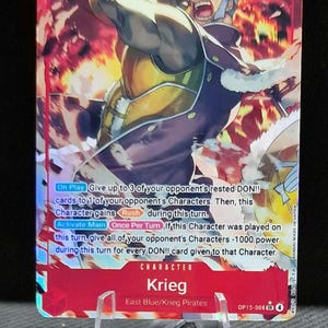 Op de afbeelding: Krieg verzamelkaart met een dynamische illustratie van een personage tegen een vurige achtergrond. De kaart toont het nummer 8, 9000 en karaktereigenschappen. De kaart wordt gepresenteerd op een transparante standaard.