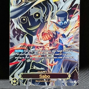 May include: A collectible Sabo character card from the One Piece card game. The card features a dynamic illustration of Sabo in action, with a top hat and goggles. The card has a power level of 9000 and a cost of 8.