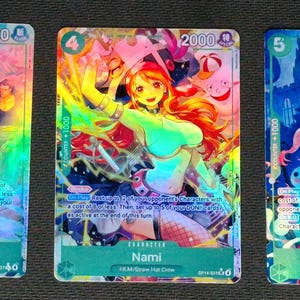 May include: Three holographic trading cards featuring anime characters. The cards display vibrant illustrations of Shanks, Nami, and Perona. Each card has a character name, numerical values, and a unique design with a green border.