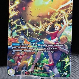 May include: A trading card depicting Zeus from the Homies/Big Mom Pirates, with a vibrant yellow and orange background and lightning effects. The card includes game instructions and a counter value of +2000. The card is held in a clear plastic stand.