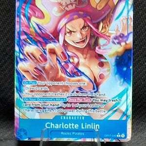 May include: A One Piece trading card featuring Charlotte Linlin with pink hair and a pirate hat. The card displays a power of 7000, a cost of 5, and text detailing game abilities including On Play and On Your Opponent's Attack effects. The card is blue.