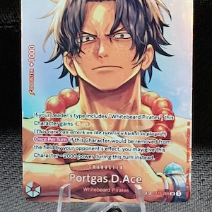 Puede incluir: Una carta coleccionable de One Piece con Portgas D. Ace, que tiene cabello oscuro, pecas y un collar de cuentas rojas. La carta muestra un nivel de poder de 6000, un coste de 5 y texto sobre mecánicas de juego de los Whitebeard Pirates.