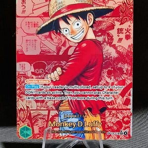 Peut inclure: Carte à collectionner de Monkey D. Luffy de One Piece. La carte est rouge et dorée, avec du texte et des illustrations japonaises. Luffy porte un chapeau de paille et une chemise rouge, souriant. La carte est sur un support transparent.