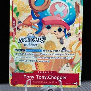 May include: A One Piece card featuring Tony Tony. Chopper, an Animal/Straw Hat Crew character. The card has a blue and brown design with the number 3 and text that reads "REGIONALS ONE PIECE CARD GAME". The card is displayed on a clear stand.